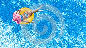 Beautiful young woman in hat in swimming pool aerial top view from above, girl in bikini relaxes and swim on inflatable ring donut