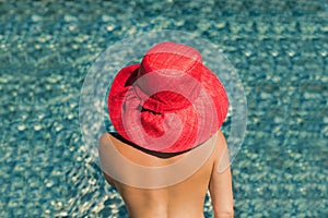 Beautiful young woman in a hat in the transparent water of the pool at sunset