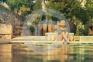 Beautiful young woman in a hat in the transparent water of the pool at sunset