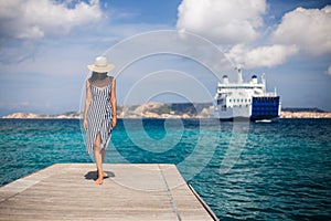 Beautiful young woman in hat walking on wooden pier on Sardinia