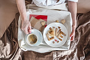 Young woman have a romantic Breakfast in morning bed. Coffee and word love from cookies. Surprise on Valentine`s day