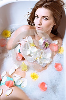 Beautiful young woman having bath with flower petals