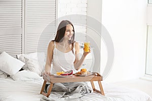 Beautiful young woman having breakfast on bed at home