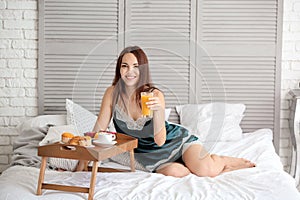 Beautiful young woman having breakfast on bed at home