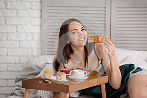 Beautiful young woman having breakfast on bed at home