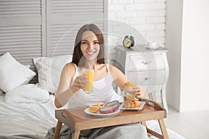 Beautiful young woman having breakfast on bed at home