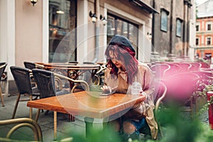 Beautiful young woman having coffee in outdoor cafe while using smartphone. Portrait of stylish girl