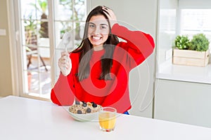 Beautiful young woman having healthy cereals and berries for breakfast stressed with hand on head, shocked with shame and surprise