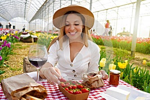 Beautiful young woman having picnic. Girl takes a strawberry. Fresh harvest in coutryside on spring time