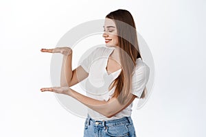 Beautiful young woman with healthy hydrated skin, holds empty space in box gesture, showing copyspace in her hands