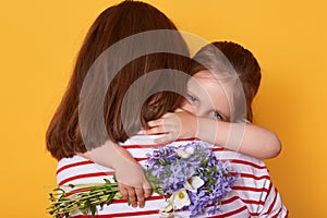 Beautiful young woman and her charming little daughter hugging indoor. Child congratulates mom with Mother`s Day, gives flowers,