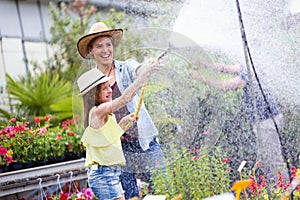 Beautiful young woman with her daughter watering the plants with a hose in the greenhouse.