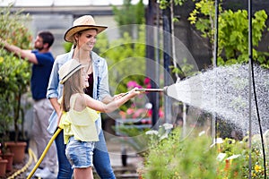 Beautiful young woman with her daughter watering the plants with a hose in the greenhouse.