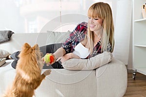 Beautiful young woman with her dog playing with ball at home.