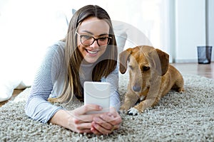 Beautiful young woman with her dog using mobile phone at home.