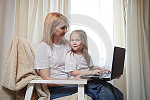 Beautiful young woman and her little cute daughter are using laptop at home. Enjoying spending time together with