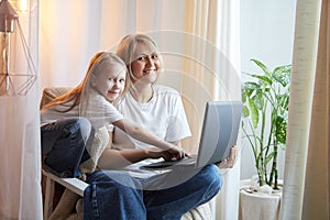 Beautiful young woman and her little cute daughter are using laptop at home. Enjoying spending time together with