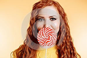 Beautiful young woman hides her mouth behind red white lollipop