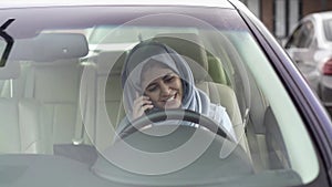 Beautiful young woman in hijab talking on smartphone in her car