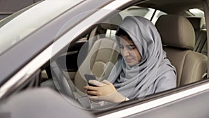 Beautiful young woman in hijab web surfing in her car, slider shot