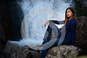 Beautiful young woman hiker sitting near waterfall