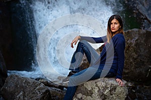 Beautiful young woman hiker sitting near waterfall