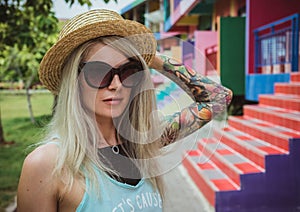 Beautiful young woman hipster with a tattoo in sunglasses and a hat on a bright coloured background. Beach style