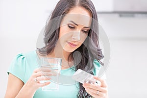 Beautiful young woman holding blister pack with pills and reading medical instructions