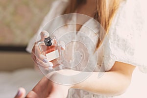 Beautiful young woman holding a bottle of perfume and applying it on her wrist