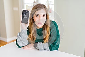 Beautiful young woman holding broken smartphone scared in shock with a surprise face, afraid and excited with fear expression