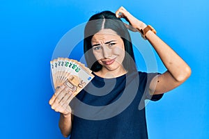 Beautiful young woman holding bunch of 50 euro banknotes confuse and wondering about question