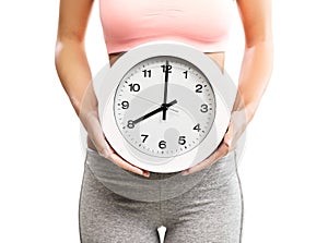 Beautiful, young woman holding a clock over her abdomen