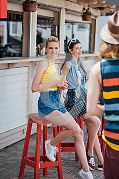 beautiful young woman holding cocktail and smiling at camera while spending time with friend photo