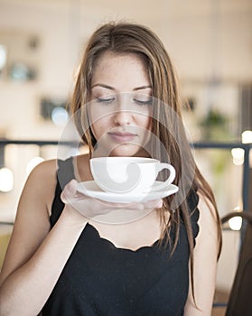 Beautiful young woman holding coffee cup and saucer at cafe