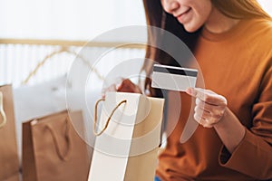 A beautiful young woman holding credit card while opening shopping bags at home