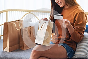 A beautiful young woman holding credit card while opening shopping bags at home