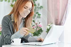 Beautiful young woman holding credit card and using laptop