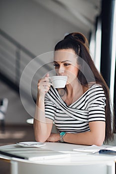 Beautiful young woman holding a cup of coffee looking away and smiling. Cheerful female enjoying a cup of coffee at cafe