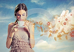 Beautiful young woman holding a cup of tea over a sky background