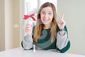 Beautiful young woman holding degree with red bow surprised with an idea or question pointing finger with happy face, number one