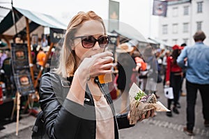 Beautiful young woman holding delicious organic salmon vegetarian burger and drinking homebrewed IPA beer on open air