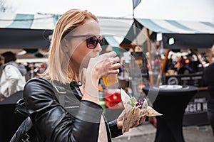 Beautiful young woman holding delicious organic salmon vegetarian burger and drinking homebrewed IPA beer on open air