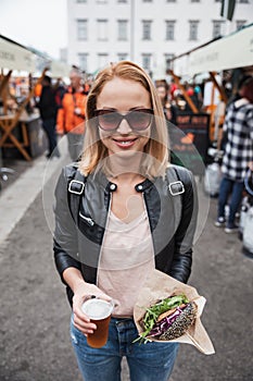 Beautiful young woman holding delicious organic salmon vegetarian burger and homebrewed IPA beer on open air beer an