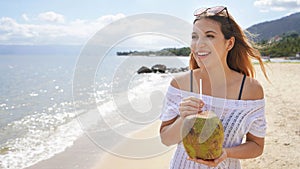 Beautiful young woman holding a fresh coconut enjoying on tropical beach. Girl relax on the beach in her travel holiday holding a