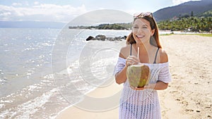 Beautiful young woman holding a fresh coconut enjoying on tropical beach. Girl relax on the beach in her travel holiday holding a