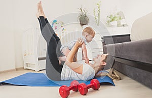 Beautiful young woman holding her baby boy and exercising on floor at home