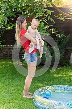 Beautiful young woman holding her baby son after swimming in inflatable pool at house backyard