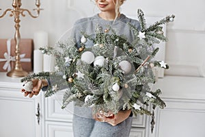 Beautiful young woman holding in her hands handmade Christmas decoration made of fir branches, fir toys, and artificial