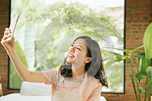 Beautiful young woman is holding a mop, using a smartphone and smiling while cleaning her house