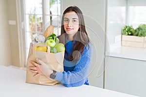 Beautiful young woman holding paper bag full of healthy groceries with a confident expression on smart face thinking serious